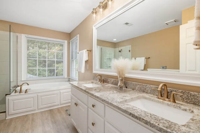 Modern bathroom remodel in Denver Colorado featuring granite double vanity, soaking bathtub, large mirror, and natural light from window.